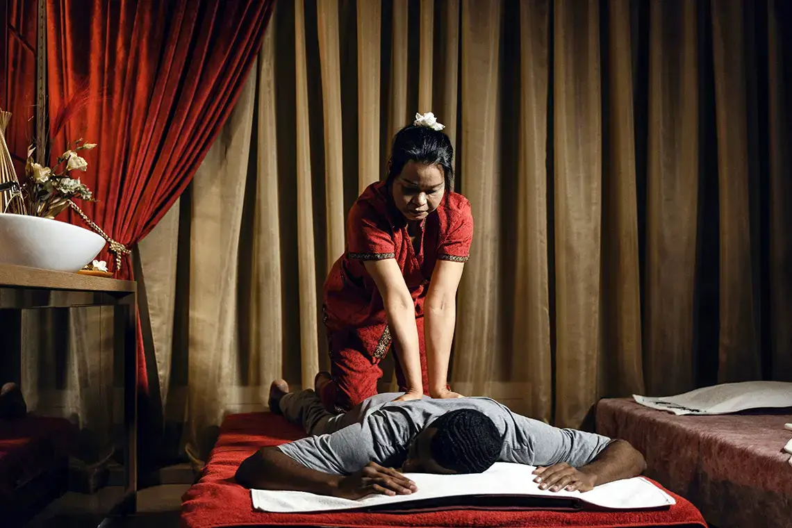 Thai Massage Diploma Program 1 Thai Massage Course - Thai Massage Diploma: A thai woman massages the back of a clothed person laying on a mat.